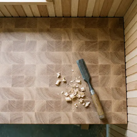 Top-down view of a wooden workbench with a chisel and sparks, showing a tidy workspace for carpentry and hands at work on a product.