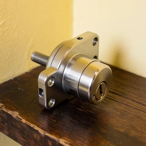 Close-up of a sturdy metal padlock resting on a wooden surface with warm lighting and a yellow wall background.