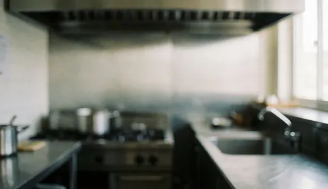 A clean, out-of-focus background suitable for adding text, featuring neutral tones and subtle hints of stainless steel surfaces typical of a professional kitchen environment.