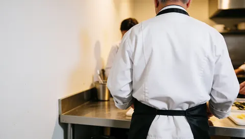 Back view of a professional chef working in a clean industrial kitchen with copy space on the left