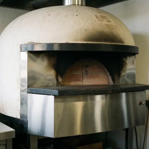 A compact wood-fired brick oven designed for commercial kitchens, featuring a metal door and a rustic interior suitable for professional pizza baking.