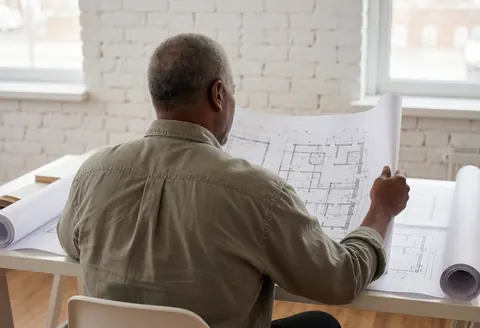 An architect reviews architectural blueprints in a modern office with white brick walls, natural light, and a professional atmosphere.