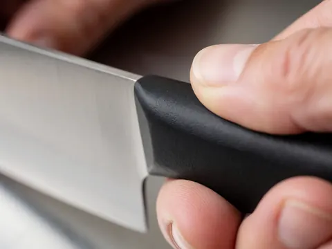 Detailed view of a black ergonomic handle on a stainless steel professional kitchen knife held in hand