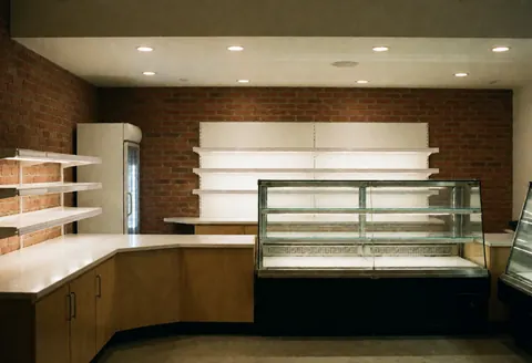 Empty and clean bakery interior with brick walls, illuminated display cases, and counters ready to open to the public.