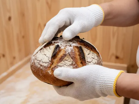 Detailed view of hands wearing gloves kneading fresh dough with flour nearby for artisan bread making