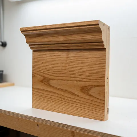 A close-up view of a single piece of natural oak crown molding showcasing its smooth finish and wood grain texture against a neutral background.