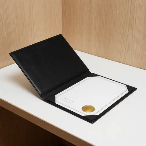 Black professional portfolio with a gold seal resting on a white desk against a wood wall in a modern office setting
