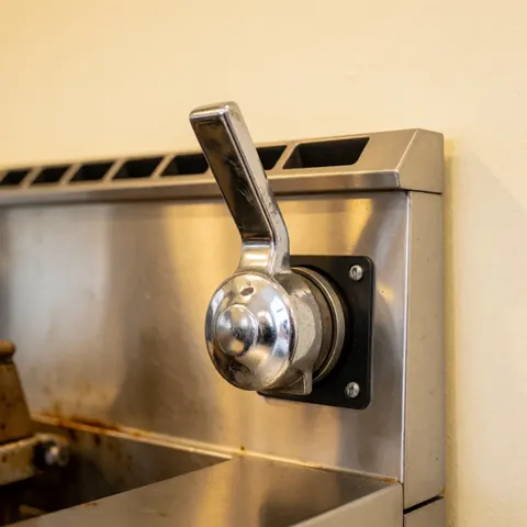 Close-up view of a stainless steel handle on a commercial kitchen oil filtration system, highlighting the metallic mechanism and professional-grade construction.