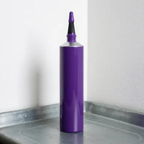 Close-up of purple PVC pipe cement in a metal tray with an applicator brush, ready for plumbing installation.