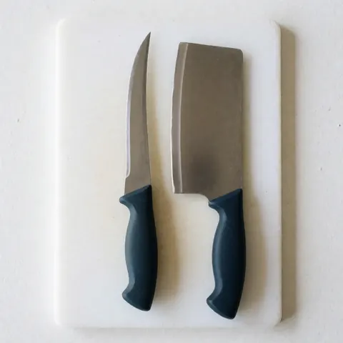 Close-up of a professional boning knife and a wooden cutting board placed on a stainless steel surface in a commercial kitchen setting
