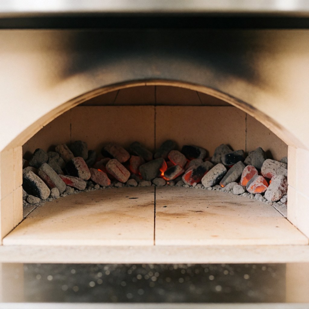 Close-up interior of a commercial wood-fired pizza oven with glowing embers and refractory stone walls used for baking.