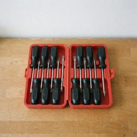 Red screwdrivers with black handles organized in an open box on a wooden workbench under natural light