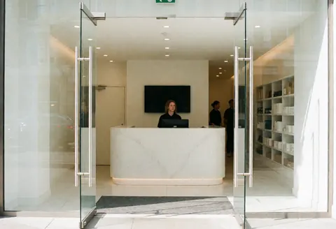 Clean and bright gym entrance featuring a minimalist reception area with glass partitions and modern furniture for a professional fitness business.