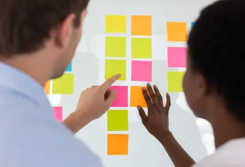 Close-up of hands placing colorful sticky notes on a wall during a collaborative team meeting to organize business ideas and tasks