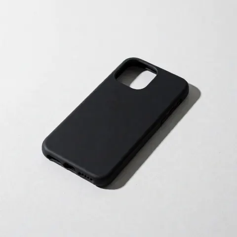 Black matte cell phone case resting on a white concrete surface with cool lighting and a defined shadow to the right, showcasing a minimalist aesthetic.