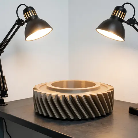 Close-up of a helical polymer gear part resting on a white workbench under warm desk lamps in a manufacturing setting