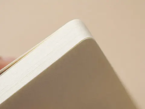 A close-up view showing the textured edge and surface of a thick paper notebook, highlighting the material quality and clean lines suitable for business documentation and office organization.