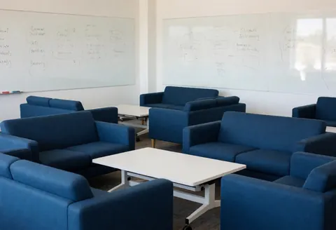 Modern conference room featuring blue sofas, white tables, and whiteboards with diagrams for team collaboration.