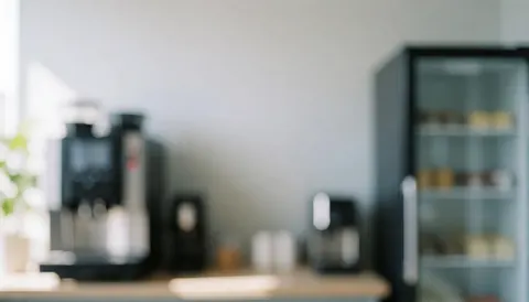 A soft focus background of a modern office break room featuring a coffee machine and refrigerator, suitable for text overlays
