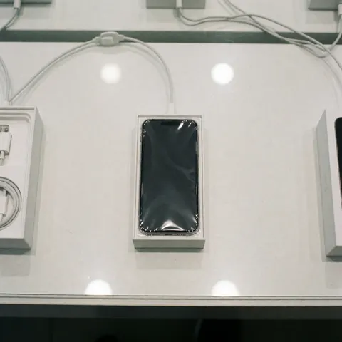 Brand new smartphone in its original packaging resting on a retail counter with a charging cable and store lighting, ready for sale.