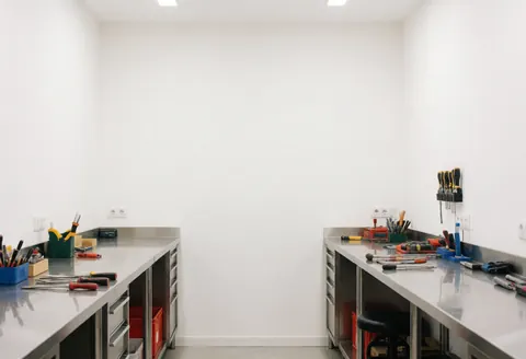 Clean minimalist electronics repair shop with stainless steel workbenches, organized tools, and white walls in a bright professional space