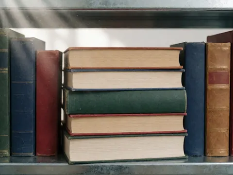 Stack of colorful university textbooks on a metal shelf illuminated by a beam of light, ideal for educational settings