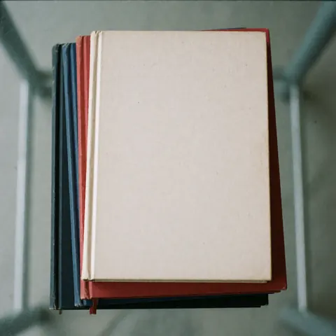Top view of a pile of colorful university textbooks on a glass surface with even lighting, representing education and study