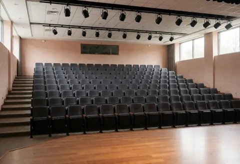 An empty university auditorium featuring rows of seats facing a stage, suitable for lectures and presentations