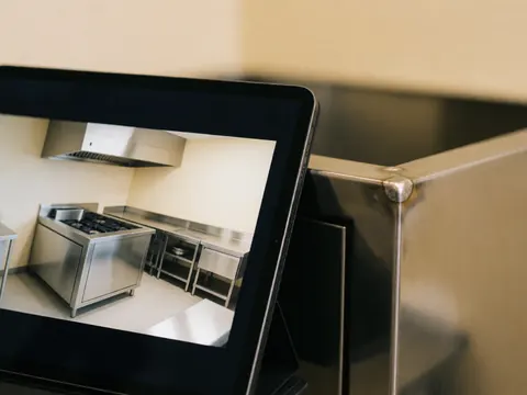 Close-up of a professional kitchen featuring a tablet, polished metal surfaces, visible welding, and commercial equipment.