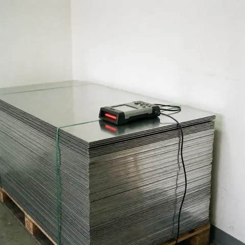 Neatly stacked metal sheets on a pallet with an industrial scanner on top, set against white walls with clean lighting for metallurgical industry use