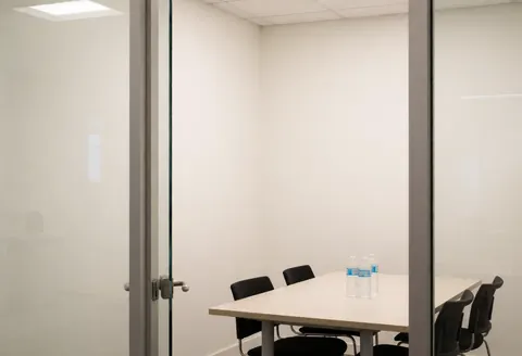 Empty minimalist conference room featuring a table, black chairs, water bottles, and white walls, suitable for nonprofit organizations and community groups.
