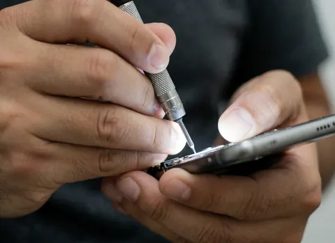 Close-up of technician hands using a precision screwdriver to open a smartphone, highlighting technical details and tools against a blurred background.