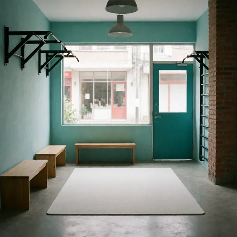 Neatly arranged fitness gear including benches and mats in a minimalist gym with turquoise walls and brick pillars