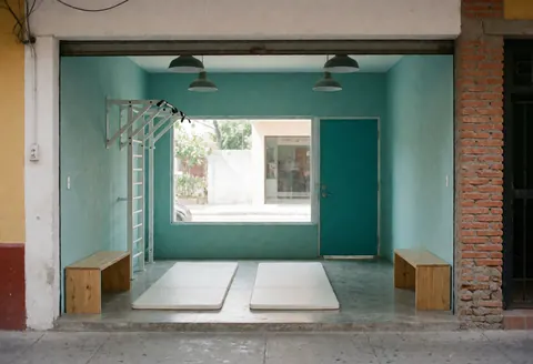 Small fitness studio featuring turquoise walls, gray flooring, wooden benches, and industrial pendant lights for workouts