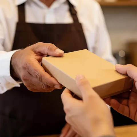 Close-up of hands holding a box containing coffee and cacao products during a delivery transaction