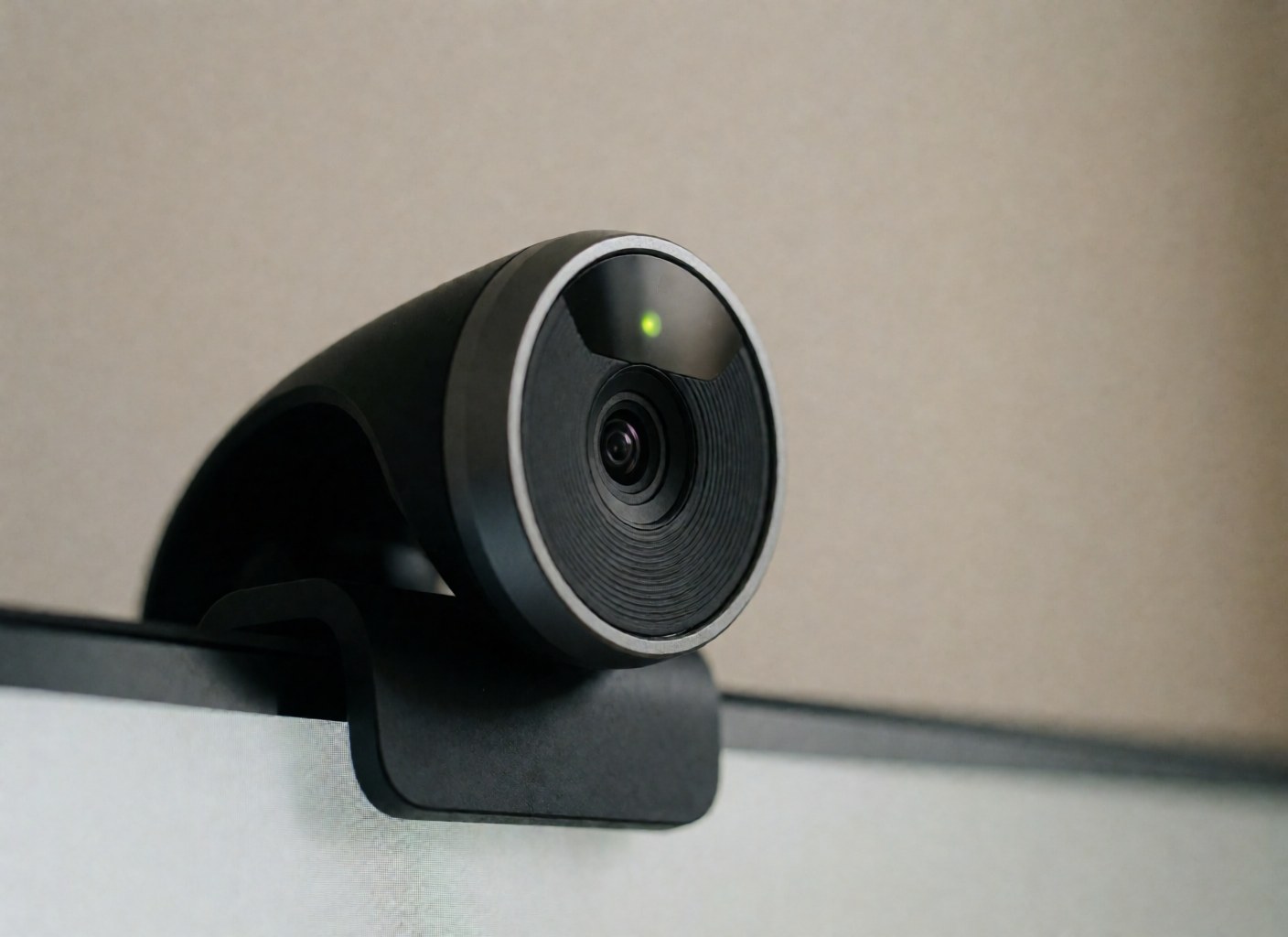 Black webcam with green light mounted on a monitor against a blurred beige background, suitable for modern office team meetings