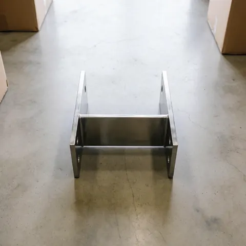 A precise polished metal bracket resting on a concrete factory floor under soft industrial lighting