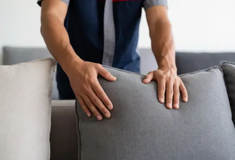 A professional technician adjusts a sofa cushion during a furniture repair service at a modern furniture store, demonstrating hands-on maintenance work.