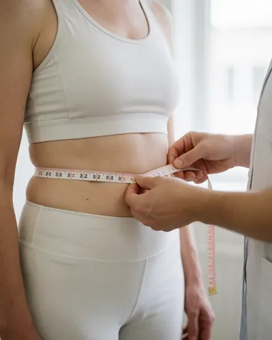 A nutritionist uses a measuring tape to check a client's waist size during a personalized health consultation in a clinical setting.