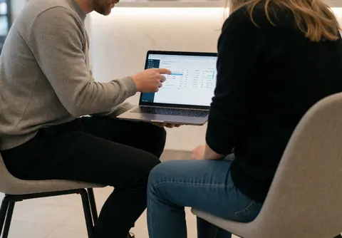 Marketing specialist explaining data on a laptop to a client in a modern reception area with professional lighting.
