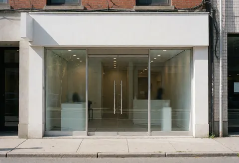 Modern glass door entrance of a professional consulting office building with clean interior visible through the glass, bright natural daylight and clear sky.