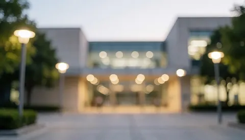 A modern university entrance at sunset featuring warm lighting and soft bokeh, providing a calm and professional background for text overlays.