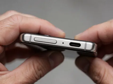 Close-up view of a smartphone showing the charging port and power button with a soft gray background and metallic industrial design details