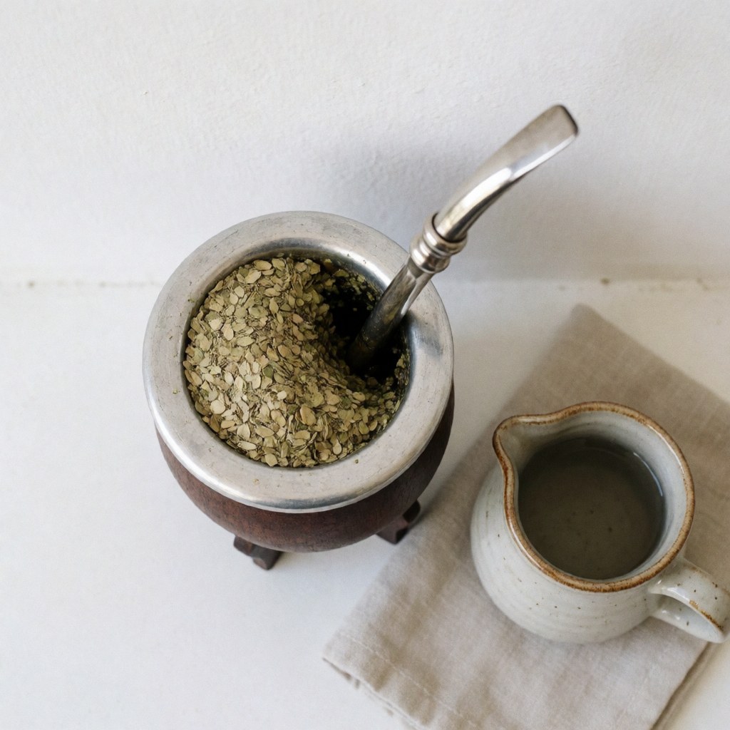 Traditional yerba mate gourd with a metal bombilla straw, a pitcher of hot water, and a cloth on a wooden table for a relaxing therapy setting