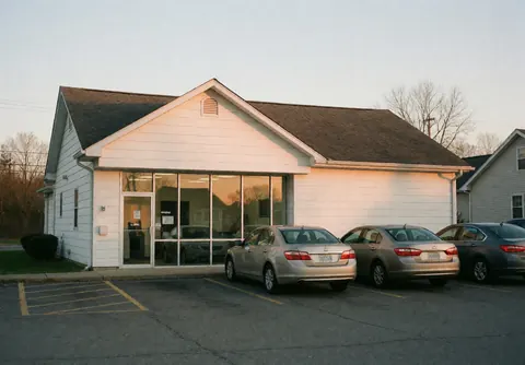 White facade insurance agency building with large window and parked cars in the lot during sunset