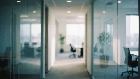 Modern office corridor featuring glass walls, blurred chairs and tables, soft lighting, and blue and white tones suitable for corporate text backgrounds.