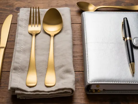 Gold utensils, silverware, napkin, and wedding planner on a wooden table for elegant event planning