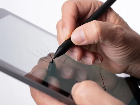 Adult hand using a black stylus on a tablet screen to create precise digital lines, showcasing professional design work against a bright white background.