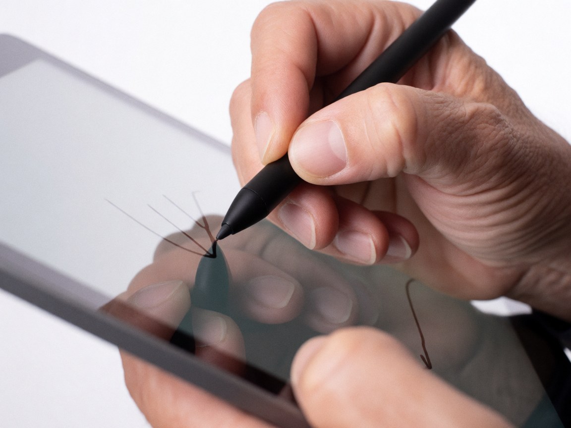 Adult hand using a black stylus on a tablet screen to create precise digital lines, showcasing professional design work against a bright white background.