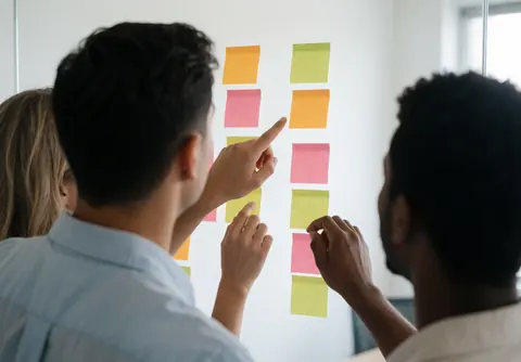 Three people organizing colorful sticky notes on a white wall during a professional team meeting.